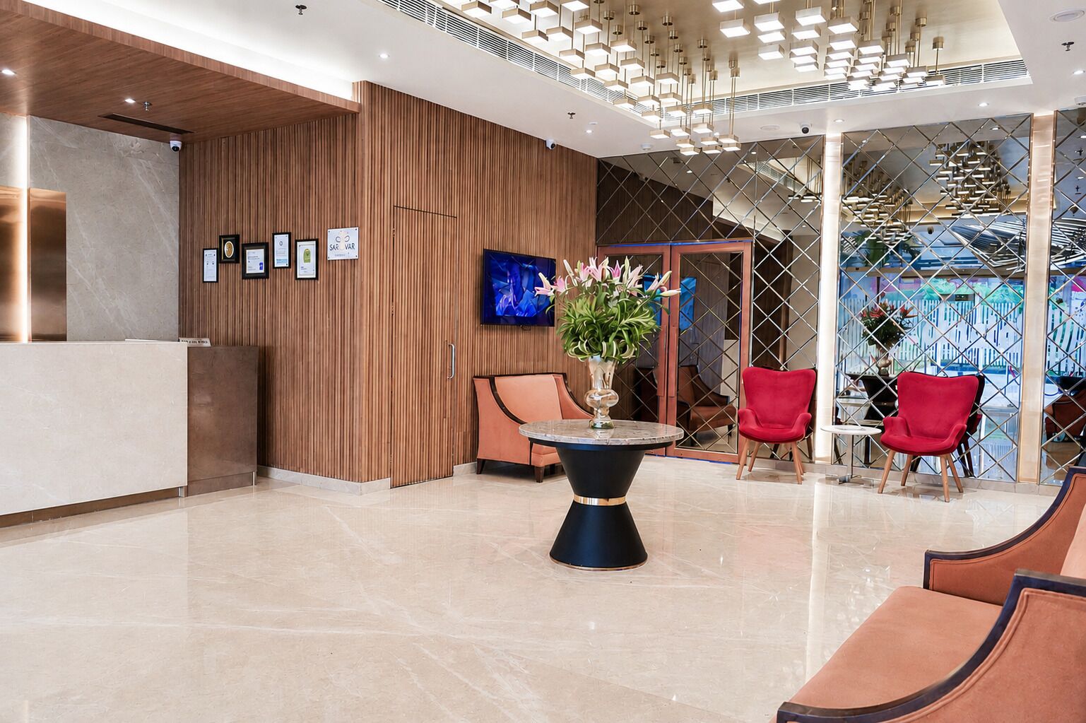 Un espace d’accueil moderne avec un mur recouvert de panneaux en bois, un comptoir d’accueil, une table ronde ornée d’un vase de fleurs et des chaises rouges.