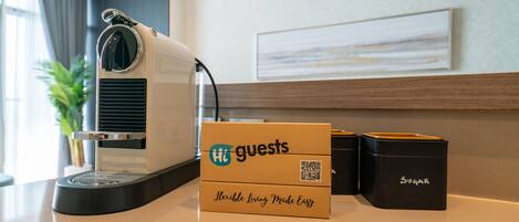 Uma máquina de café, uma caixa com a etiqueta 'Hi Guests' e dois recipientes em uma bancada.