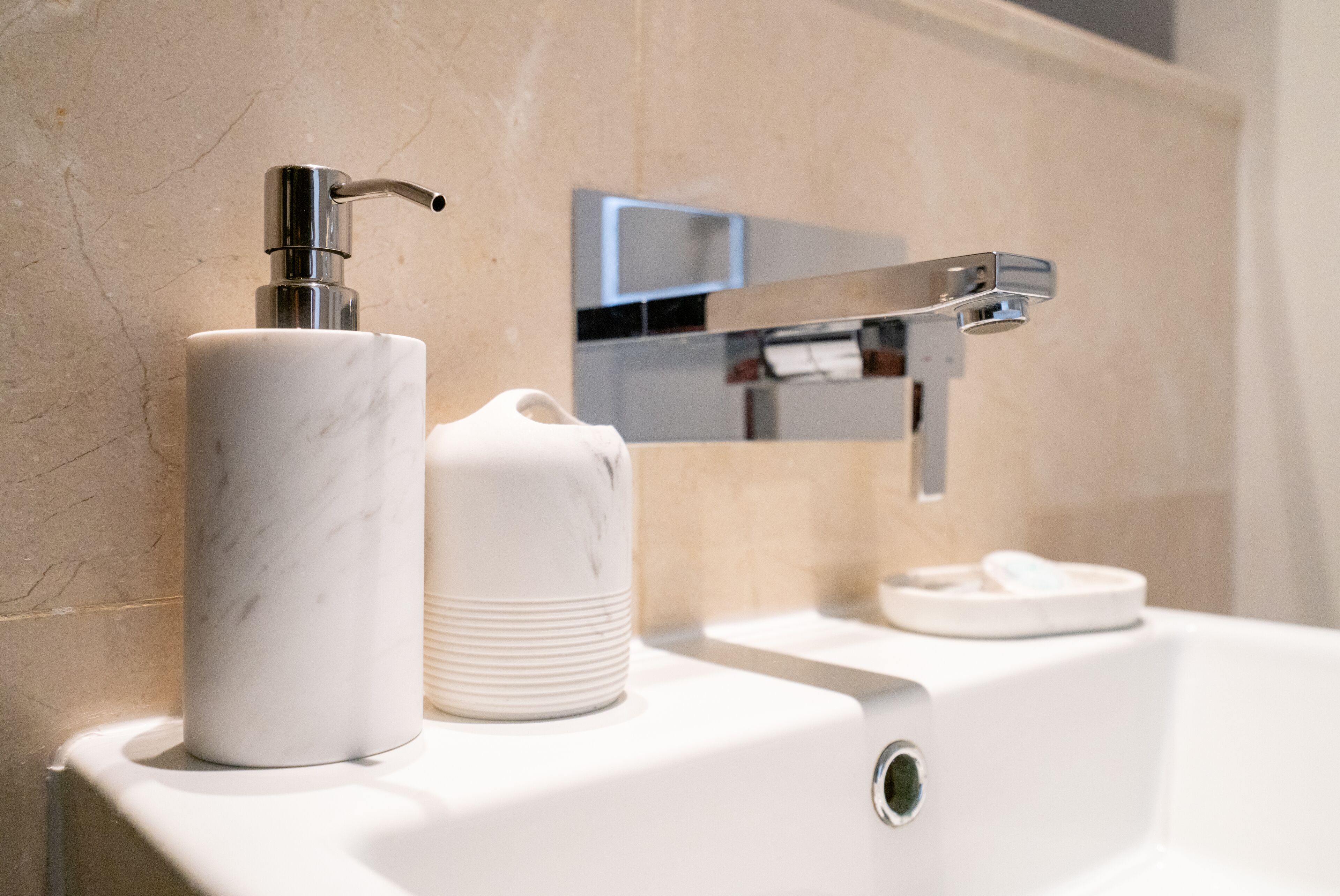 A bathroom with a marble sink, a soap dispenser, and a chrome faucet.