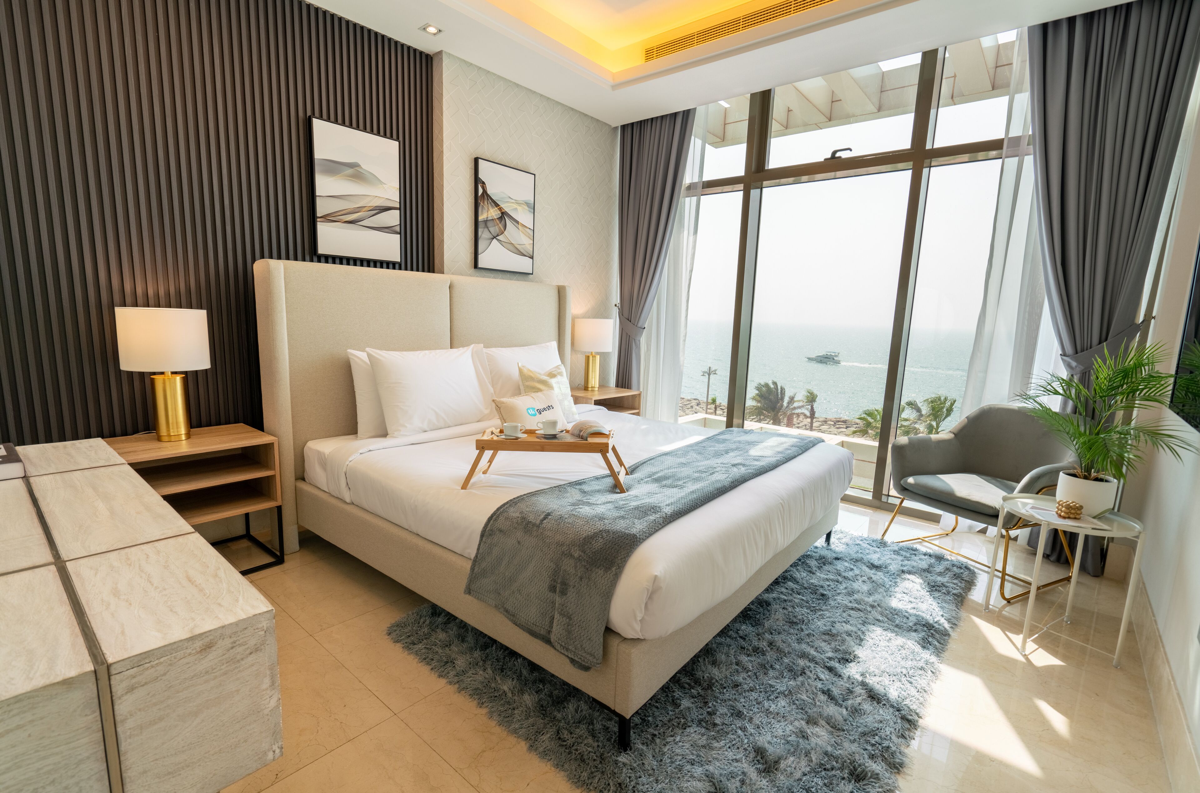 A modern hotel room with a large bed, a desk, a chair, and a view of the sea.
