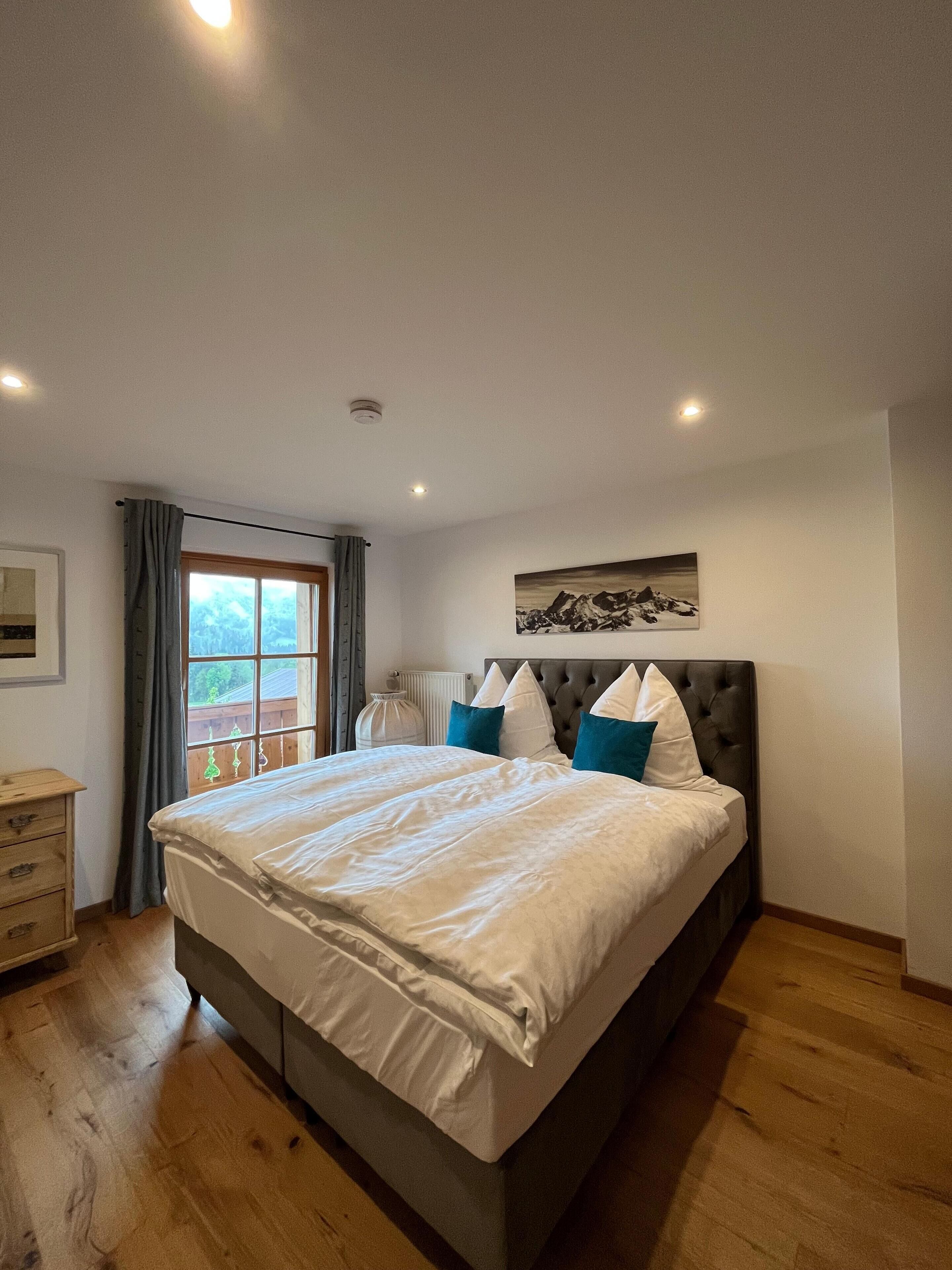 Une chambre à coucher avec un grand lit, une commode, une fenêtre avec des rideaux et un tableau au mur.