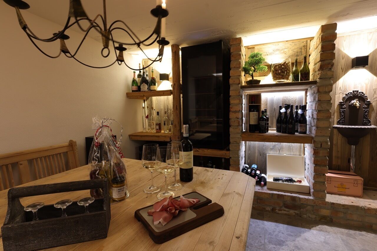 Une table de salle à manger en bois, avec des bouteilles de vin, des verres et un plateau de jambon de Parme.