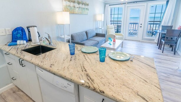 A kitchen with a sink, countertop, and a dining area with a table and chairs. - Beachsid Bungalow @ Victorian Sleeps 8 (Galveston)
