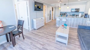 A modern kitchen with white cabinets, a dining area with a table and chairs, and a living area with a sofa. - Beachsid Bungalow @ Victorian Sleeps 8 (Galveston)