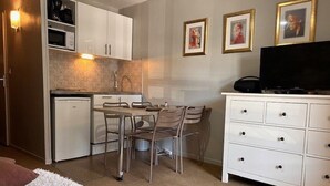 A compact kitchen with a dining table and chairs, a small refrigerator, and a white cabinet with drawers. - Cozy Studio for 4 with Ski Lift Access and South-Facing Balcony (Risoul)