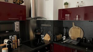 Een moderne keuken met rode kastjes, een roestvrijstalen afzuigkap, een inbouwoven, een koffieapparaat en diverse keukengerei.