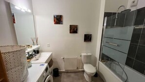 Een badkamer met een wit wastafelmeubel, toilet, wasmachine en een douchecabine van glas.