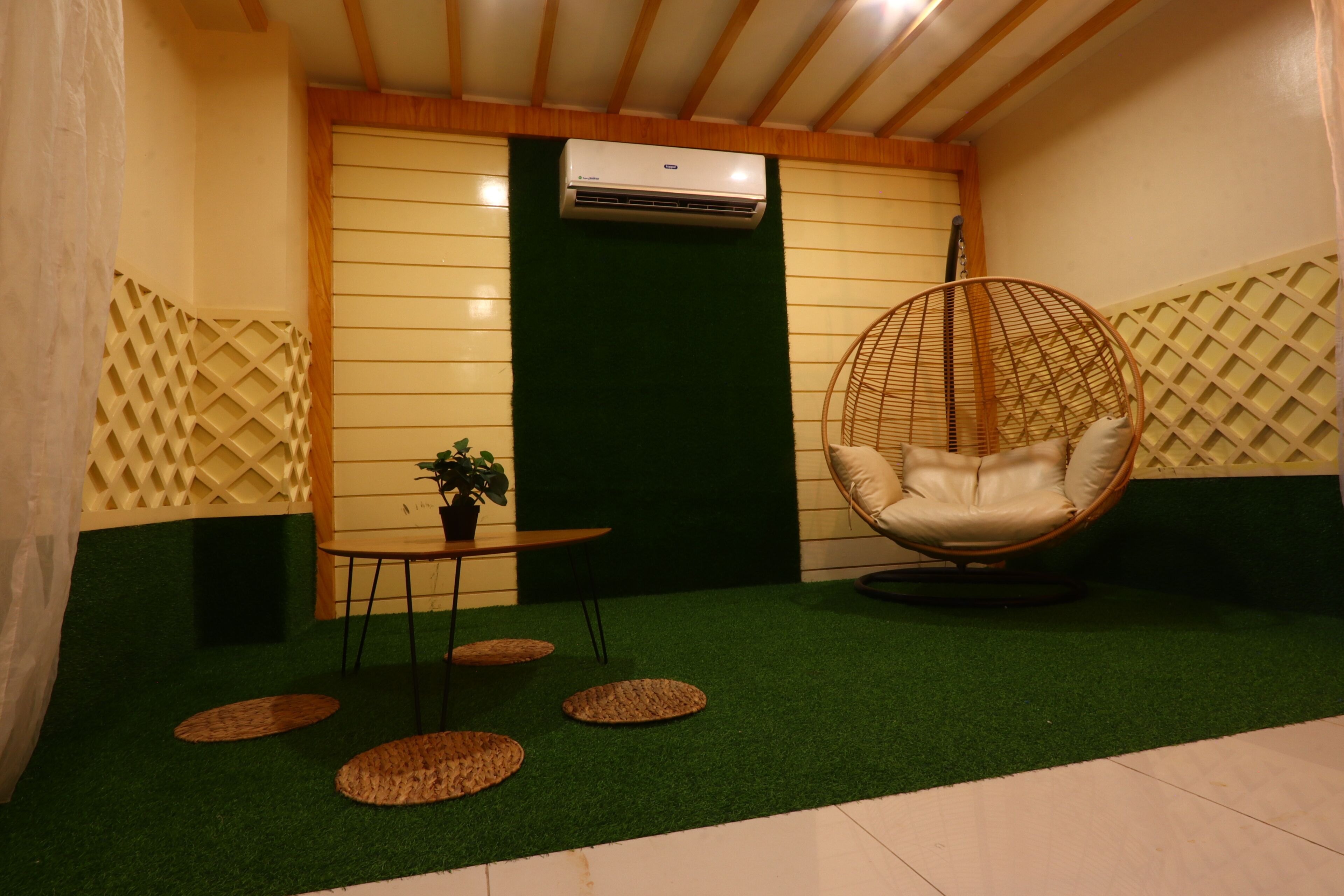Een kamer met een vloer van kunstgras, een hangstoel, een tafeltje met een plant en een luchtverfrisser aan de muur.
