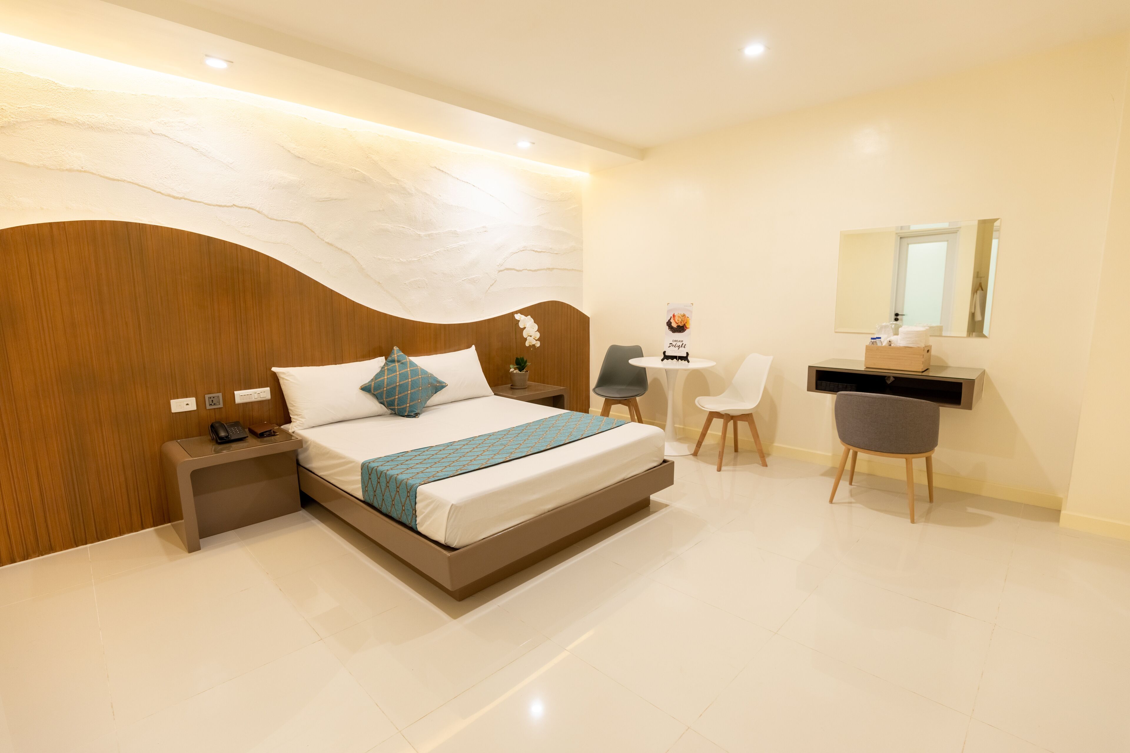 Una habitación de hotel moderna con una cama grande, mesita de noche, escritorio, silla y un espejo.