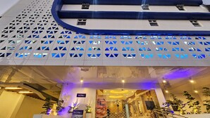 Un edificio moderno con una fachada geométrica distintiva, varios niveles y un área de entrada bien iluminada con plantas en macetas y señalización.