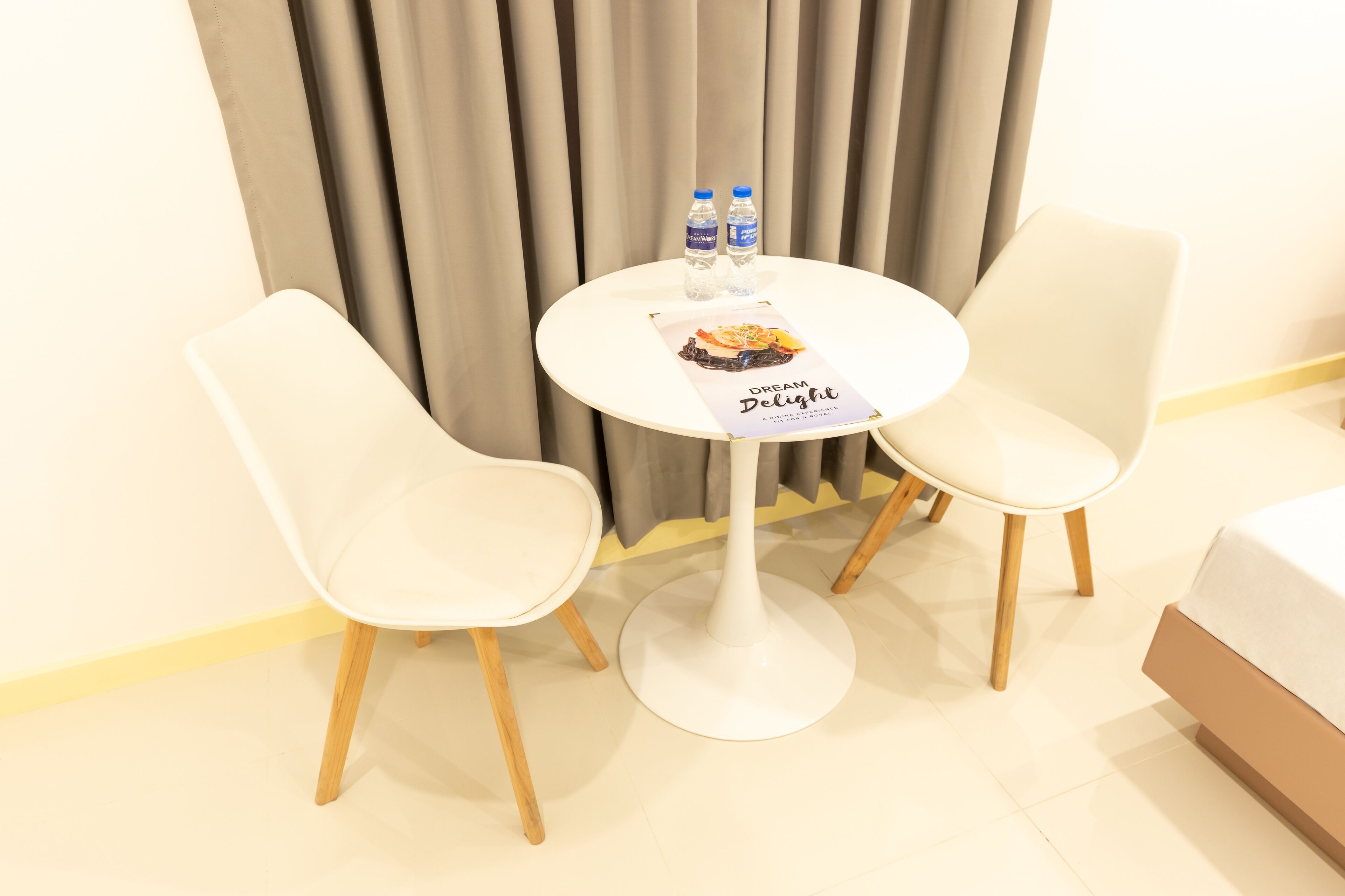 Une petite table ronde blanche, accompagnée de deux chaises blanches, et une affiche intitulée « Rêve ensoleillé ». Deux bouteilles d’eau sont posées sur la table.