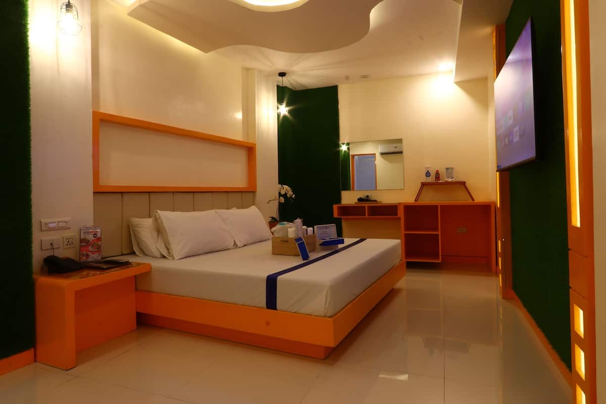 A modern bedroom with a bed, bedside table, dresser, and a TV mounted on the wall.