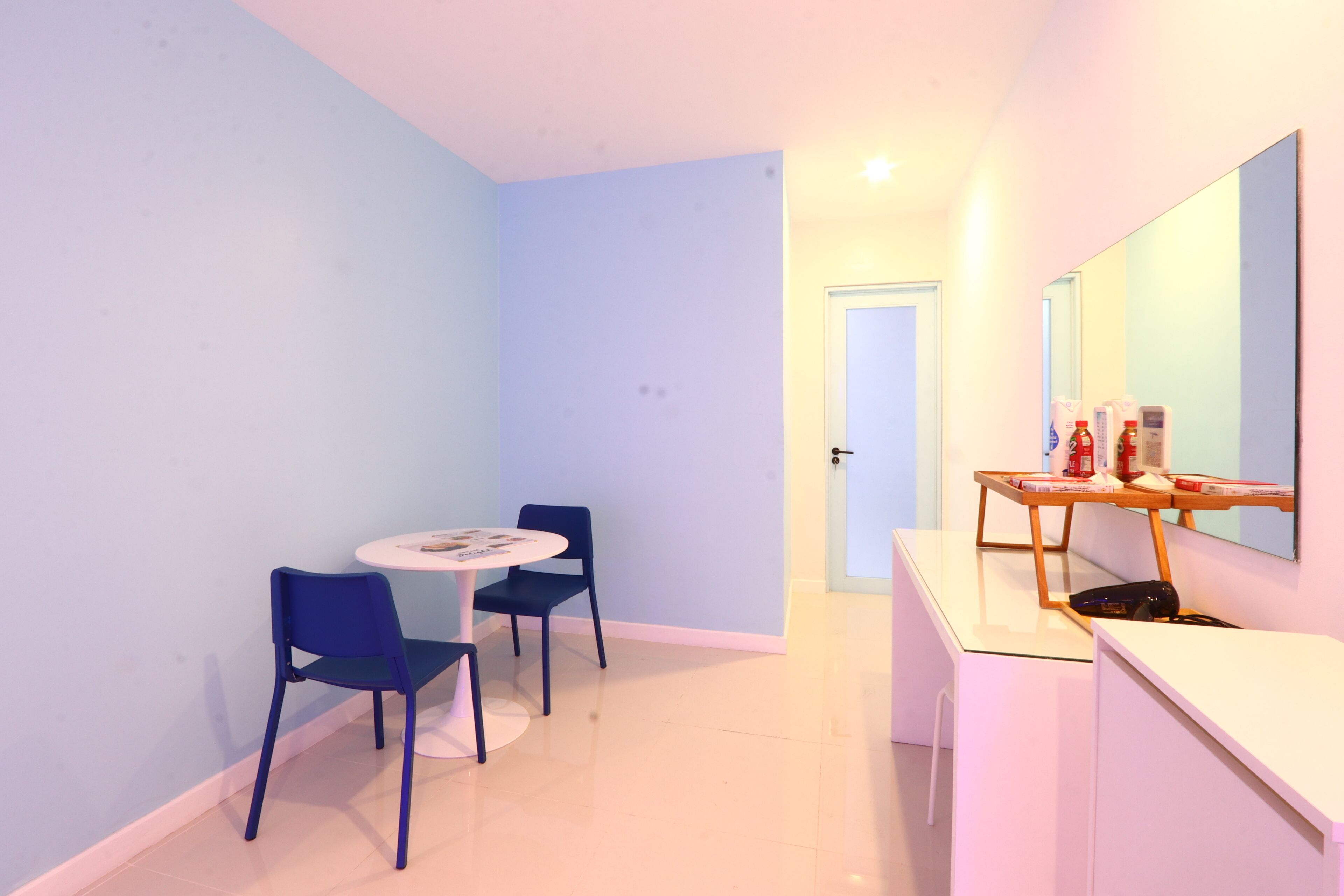 Habitació petita i ben il·luminada amb taula rodona i dues cadires, escriptori de fusta amb mirall, i una porta que dona a una altra habitació.