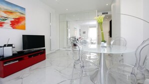 Un comedor moderno con una mesa y sillas de vidrio, un mueble de entretenimiento rojo y un cuadro grande en la pared.