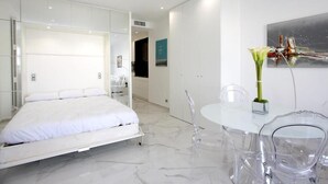 Un dormitorio moderno con cama, una mesita de cristal y un florero con flores.