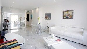 Una sala de estar moderna con un sofá blanco, una mesa de centro y un comedor con sillas traslúcidas.