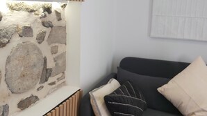 A room with a stone wall, a radiator, a grey sofa with cushions, and a framed picture on the wall.