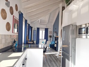 A modern kitchen with a built-in microwave, a stainless steel refrigerator, and a dining area with blue curtains and a white table. - Beautiful duplex with private terrace, 2 bedrooms - Málaga Center (Málaga)