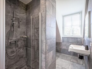 Enjoy a refreshing shower in the sleek shower with handheld showerhead and wall-mounted faucet, adjacent to a modern sink with curved faucet.
