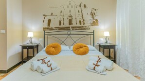 Habitación de hotel con cama, dos mesitas de noche con lámparas, un mural en la pared y toallas sobre la cama.