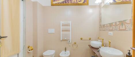 A bathroom with two sinks, a bidet, a toilet, a towel rack, and a mirror.