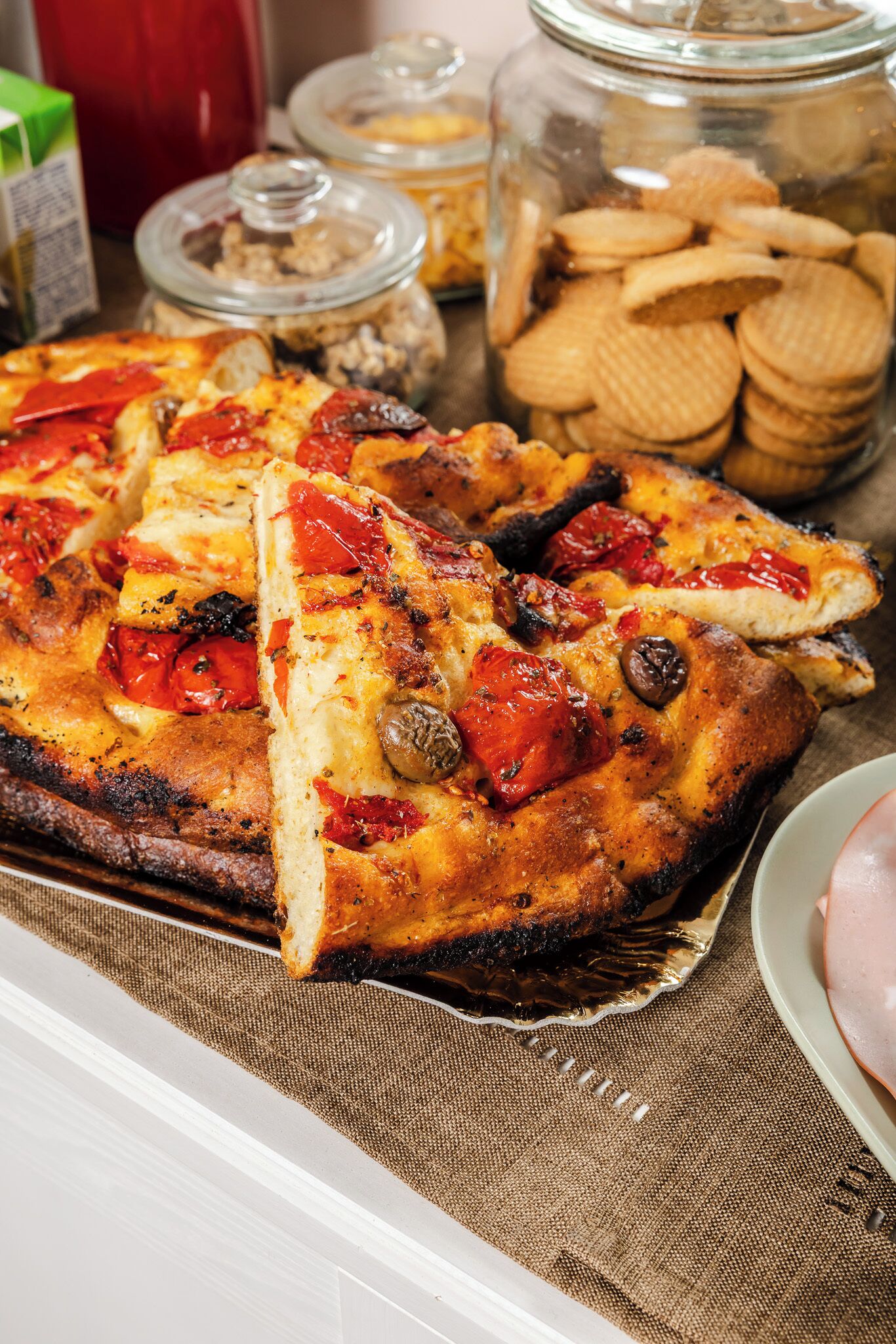 Una pizza con condimenti, un barattolo di biscotti e un piatto di prosciutto.
