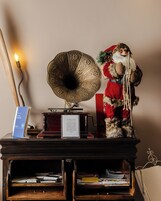 Un grammofono vintage su un supporto di legno, con un cartello, un orsetto di peluche e un albero di Natale.