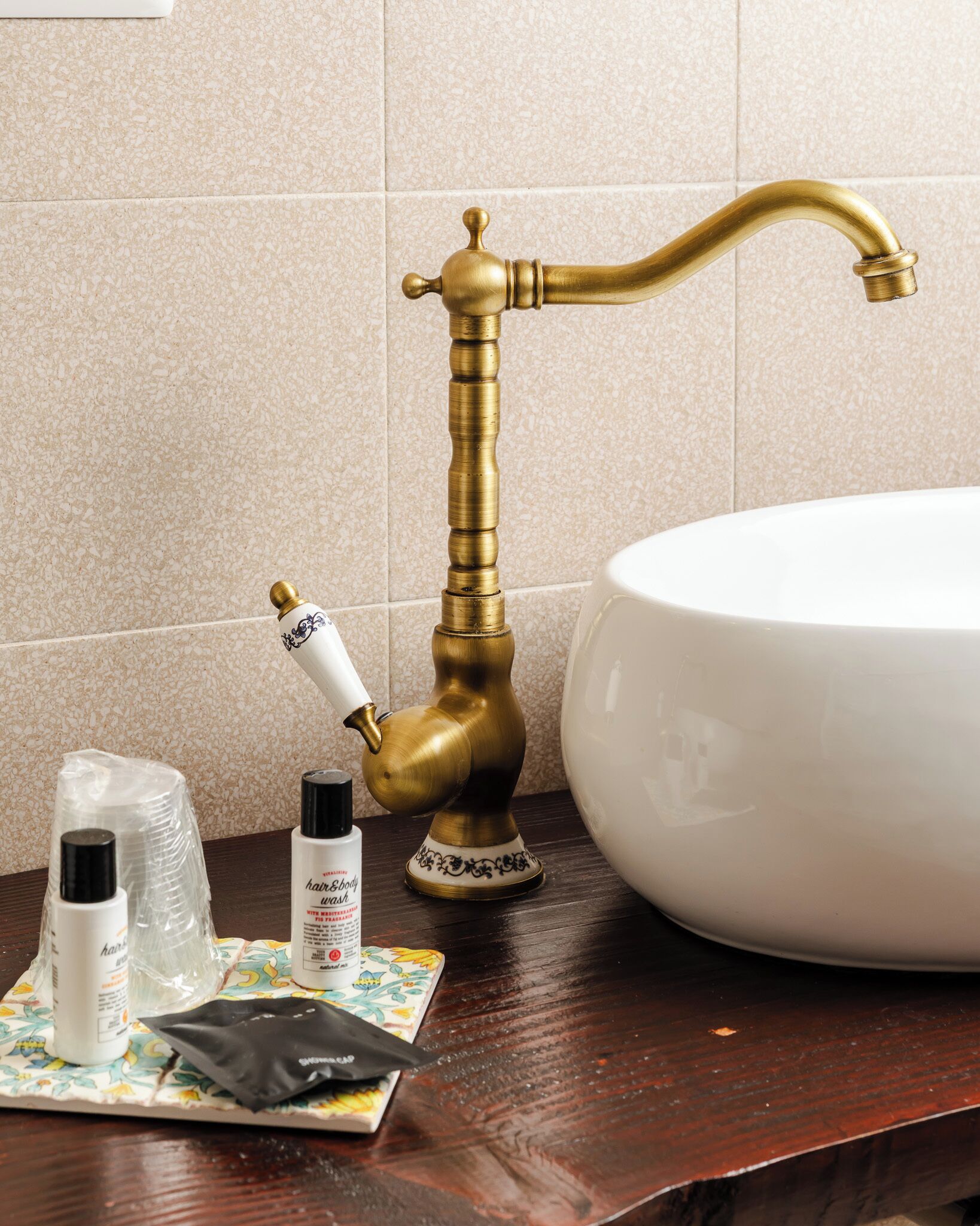 Une salle de bain avec un robinet en laiton d’époque, un lavabo blanc et des articles de toilette disposés sur une surface en bois.