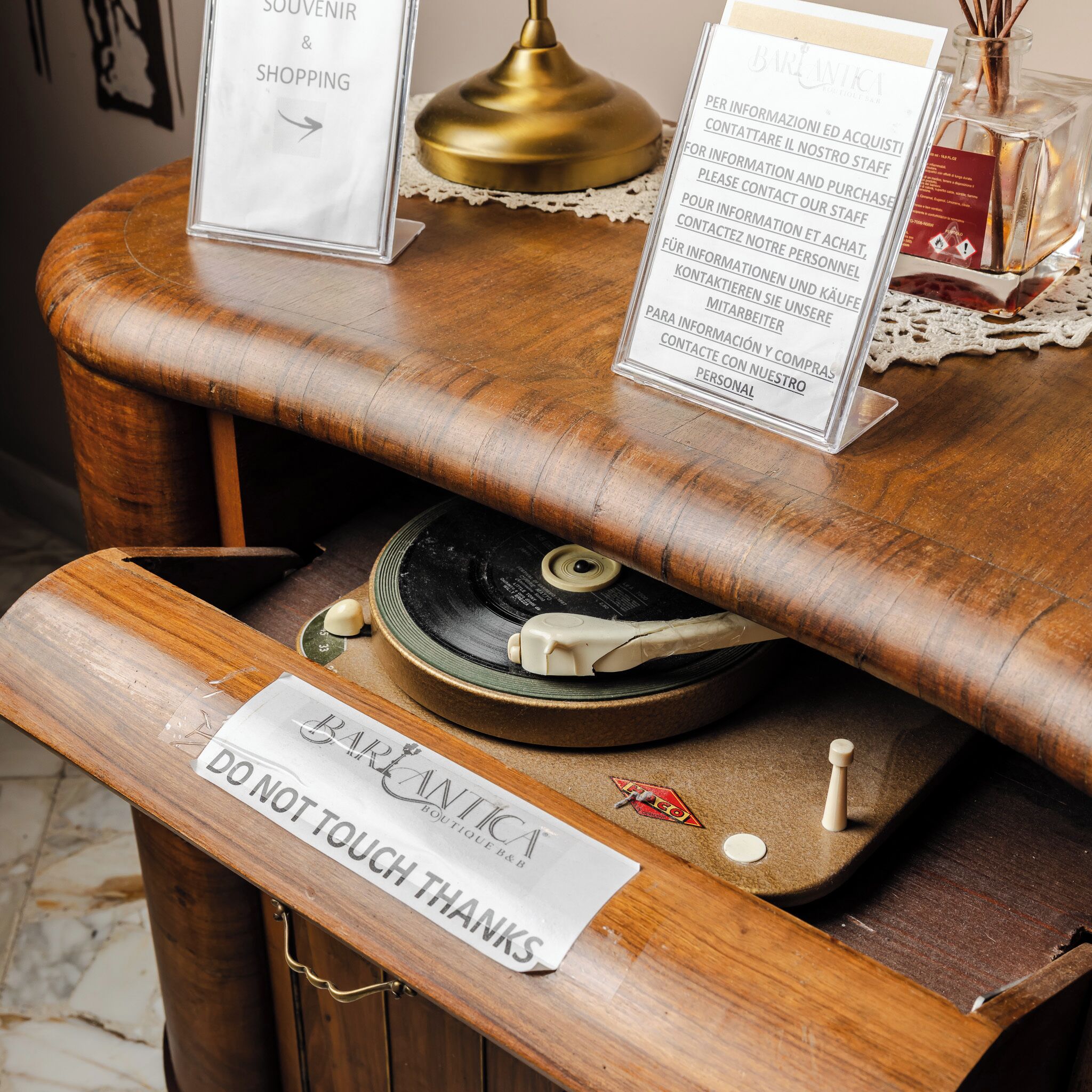 Una barra de madera con un tocadiscos antiguo, un cartel que dice 'NO TOCAR, GRACIAS' y carteles informativos en varios idiomas.