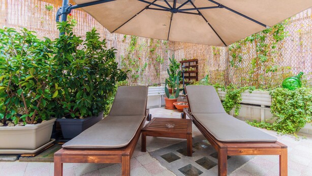 Un patio con dos sillones de madera, una mesita y una sombrilla grande.