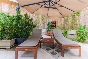 A patio area with two wooden lounge chairs, a small table, and a large umbrella. - Bari Antica Boutique B&B (Bari)