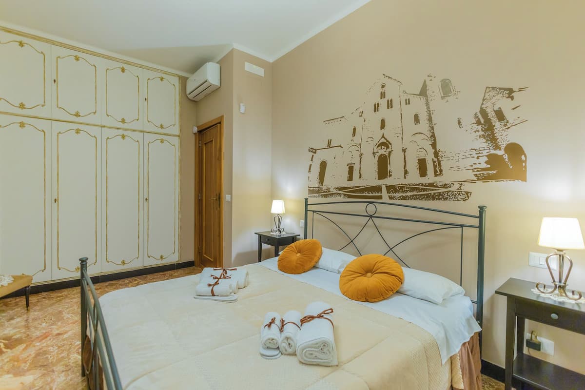 A hotel room with a bed, a wardrobe, a nightstand, and a wall mural.