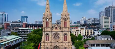 A large cathedral with two tall spires, surrounded by modern buildings and trees.