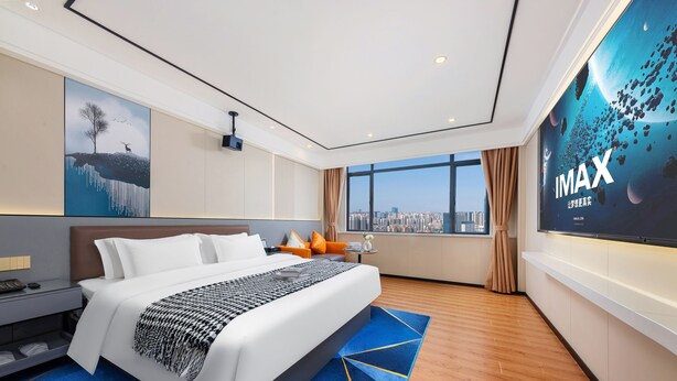 A modern hotel room with a large bed, a city view, a projector screen, and a blue patterned rug. - Xinghe Yuezhi·S Hotel (Guangzhou Yuexiu Park Railway Station Subway Station Baima Clothing City Flagship Store) (Guangzhou)