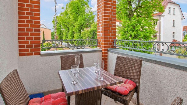A balcony with a table and wicker chairs, overlooking a residential area with trees and houses. - Gorgeous apartment in Waren (Müritz) (Waren (Müritz))