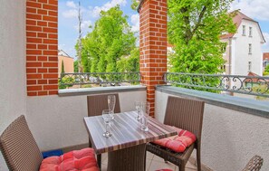 Ein Balkon mit Tisch und Korbstühlen, mit Blick auf eine Wohngegend mit Bäumen und Häusern.