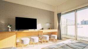 Una habitación de hotel con cama, escritorio con televisor y un ventanal grande.