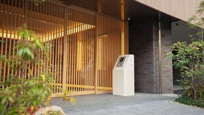 Una entrada moderna a un edificio con un portón de listones de madera, un muro de ladrillo y un quiosco digital.