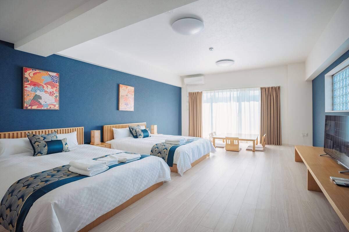 A hotel room with two beds, a TV, a desk, and a window with curtains.