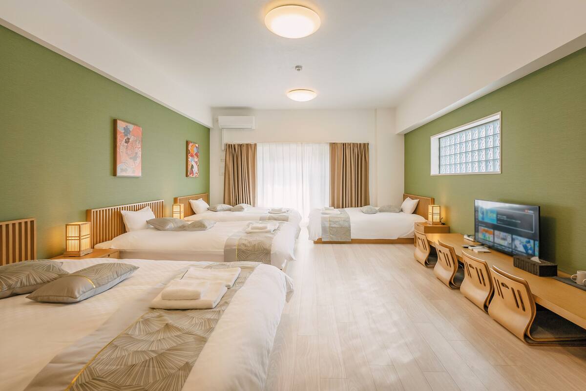 A hotel room with two beds, a TV, a desk with chairs, and artwork on the walls.