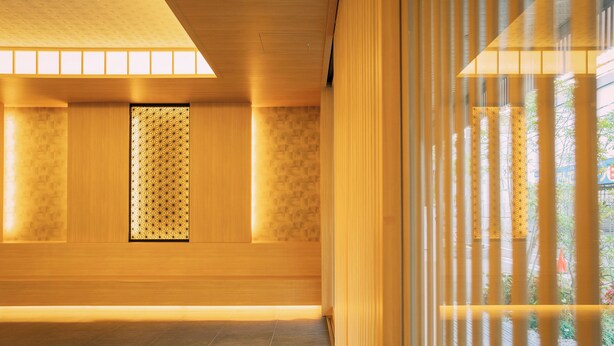 Un interior moderno con paneles de madera, un papel tapiz estampado y vistas a través de una ventana con persianas verticales.
