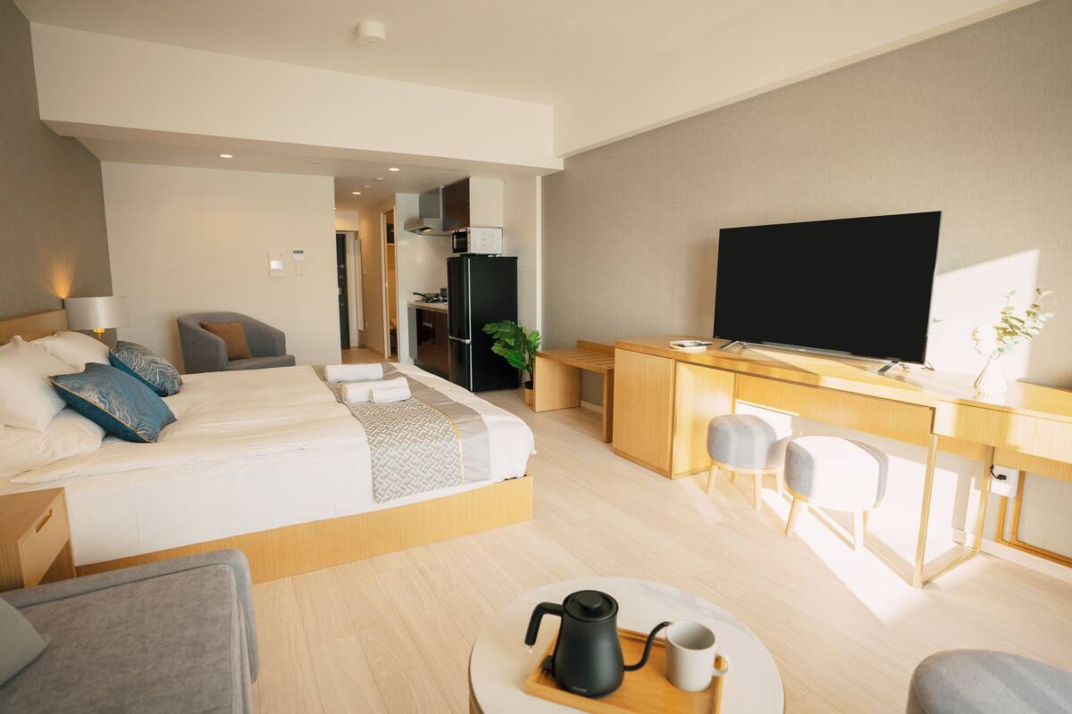 A modern hotel room with a bed, desk, TV, and seating area.