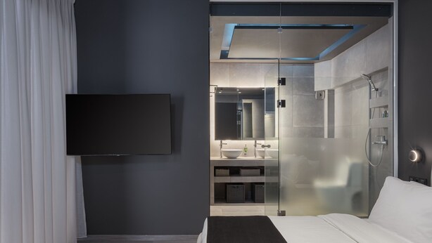 A modern hotel room with a large bed, a flat-screen TV, a glass-enclosed shower, and a bathroom with a sink and mirror. - The Riviera Hideaway (Vari-Voula-Vouliagmeni)