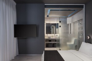 A modern hotel room with a large bed, a flat-screen TV, a glass-enclosed shower, and a bathroom with a sink and mirror. - The Riviera Hideaway (Vari-Voula-Vouliagmeni)