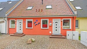 Ein zweistöckiges Gebäude mit roter Fassade, nummerierten Hauseingängen und einem Ziegeldach.