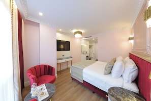 A hotel room with a bed, a red armchair, a small table with a tray of food, a desk with a mirror, and a television. - Golden Horn Bosphorus Hotel (Istanbul)