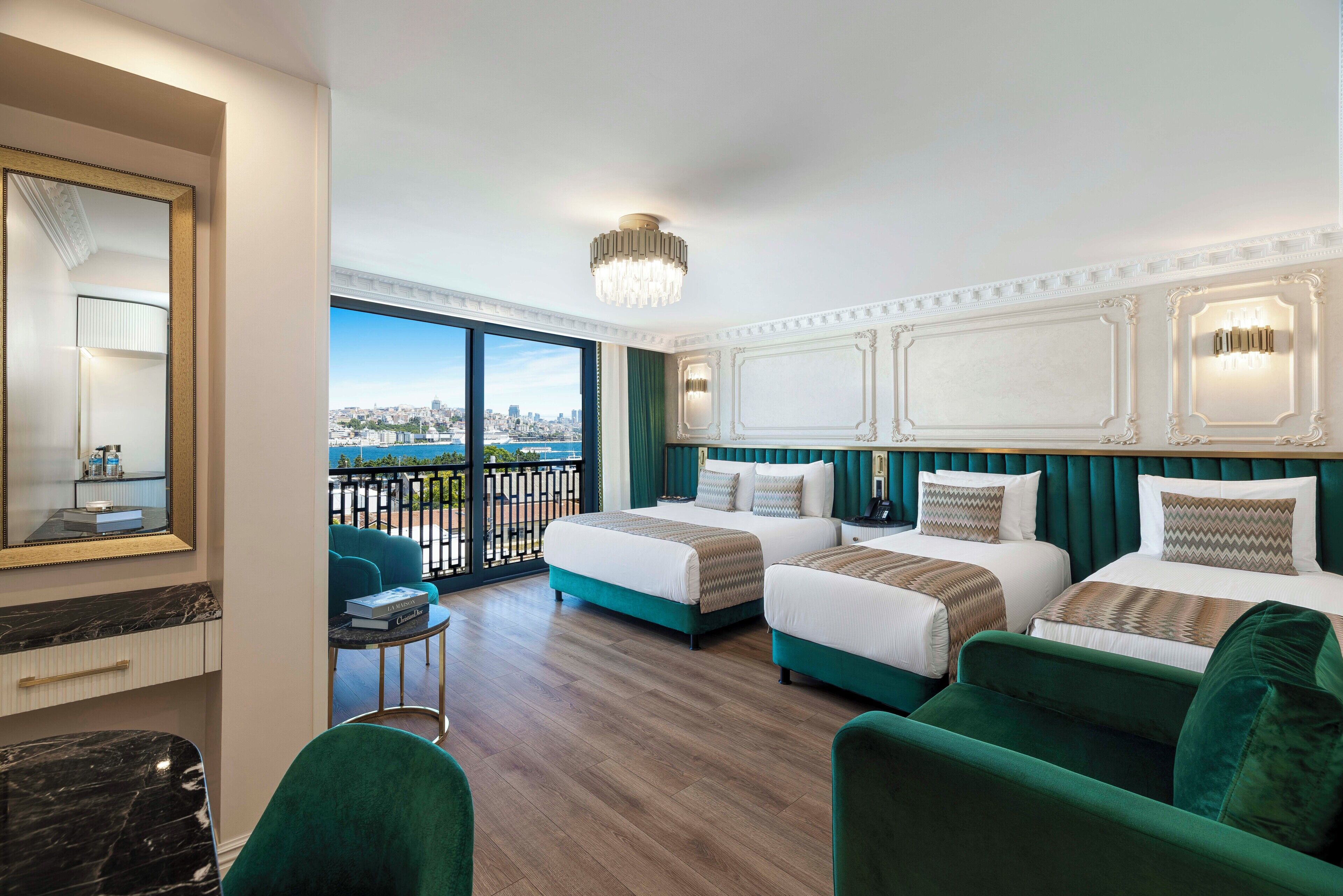 Habitación de hotel con dos camas, un balcón con vista a la ciudad, una mesa redonda y un espejo grande.