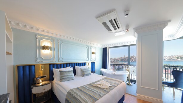 A hotel room with a large bed, a nightstand with a phone, a bathtub, and a view of a cityscape. - Golden Horn Bosphorus Hotel  (Istanbul)