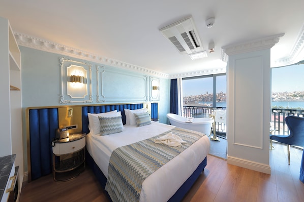 A hotel room with a large bed, a nightstand with a phone, a bathtub, and a view of a cityscape. - Golden Horn Bosphorus Hotel (Istanbul)
