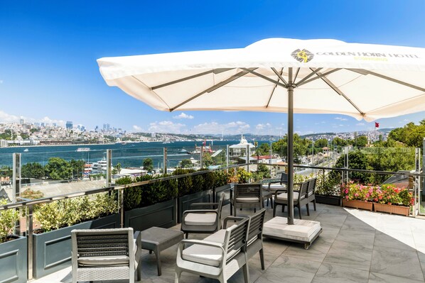 A terrace with outdoor seating, a view of the city, and a large umbrella.